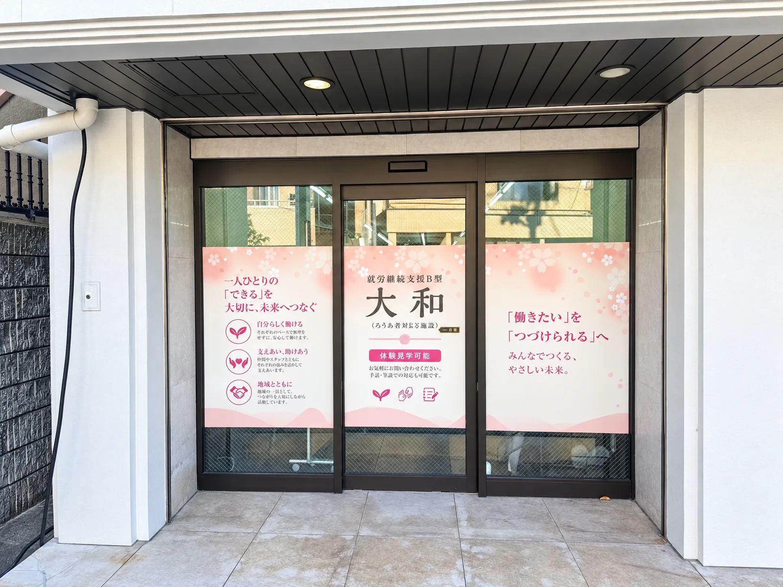 就労継続支援B型 大和の入口外観。桜色の案内サインがあるガラス扉